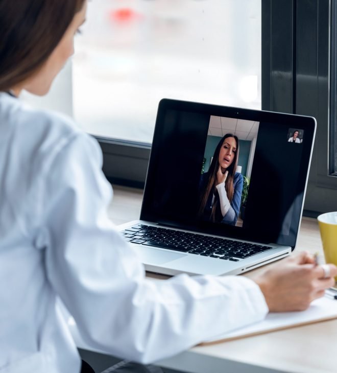 Shot of back view of a doctor attending to a woman patient through a video call with the laptop at home.